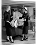 1950s woman in hat stole & gloves taking hatbox from saleswoman by Anonymous