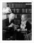 1930s 1940s retired senior couple looking at check in living room man smoking pipe by Anonymous