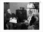 1930s elderly couple sitting in living room listening to radio woman knitting man with newspaper in lap by Anonymous