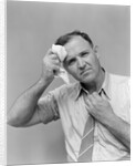 1940s 1950s perspiring man in rolled up shirt sleeves loosening tie holding handkerchief wiping forehead looking at camera by Anonymous