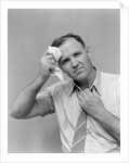 1940s 1950s perspiring man in rolled up shirt sleeves loosening tie holding handkerchief wiping forehead looking at camera by Anonymous