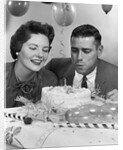 1950s 1960s couple with birthday anniversary cake man blowing out candle by Anonymous