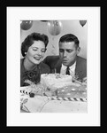 1950s 1960s couple with birthday anniversary cake man blowing out candle by Anonymous