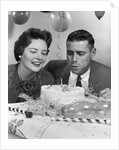 1950s 1960s couple with birthday anniversary cake man blowing out candle by Anonymous