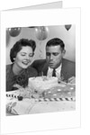1950s 1960s couple with birthday anniversary cake man blowing out candle by Anonymous