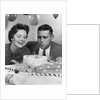 1950s 1960s couple with birthday anniversary cake man blowing out candle by Anonymous