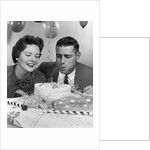 1950s 1960s couple with birthday anniversary cake man blowing out candle by Anonymous