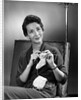 1950s woman crocheting baby sock looking at camera by Anonymous