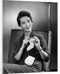 1950s woman crocheting baby sock looking at camera by Anonymous