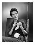 1950s woman crocheting baby sock looking at camera by Anonymous