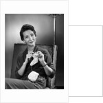 1950s woman crocheting baby sock looking at camera by Anonymous