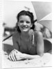 1930s teen girl lying on beach under umbrella wearing bathing suit smiling looking at camera by Anonymous