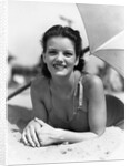 1930s teen girl lying on beach under umbrella wearing bathing suit smiling looking at camera by Anonymous