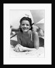 1930s teen girl lying on beach under umbrella wearing bathing suit smiling looking at camera by Anonymous