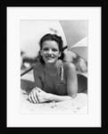 1930s teen girl lying on beach under umbrella wearing bathing suit smiling looking at camera by Anonymous