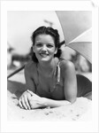 1930s teen girl lying on beach under umbrella wearing bathing suit smiling looking at camera by Anonymous