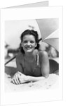 1930s teen girl lying on beach under umbrella wearing bathing suit smiling looking at camera by Anonymous