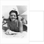 1930s teen girl lying on beach under umbrella wearing bathing suit smiling looking at camera by Anonymous