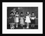 1930s line-up of 5 elementary school students in front of blackboard reading books with teacher looking on by Corbis