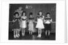 1930s line-up of 5 elementary school students in front of blackboard reading books with teacher looking on by Anonymous
