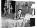 1940s fully dressed smiling woman laying on her bed with her legs up reading a letter in her bedroom by Anonymous