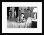 1940s fully dressed smiling woman laying on her bed with her legs up reading a letter in her bedroom by Anonymous