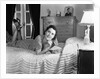 1940s fully dressed smiling woman laying on her bed with her legs up reading a letter in her bedroom by Anonymous