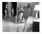 1940s fully dressed smiling woman laying on her bed with her legs up reading a letter in her bedroom by Anonymous