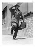 1960s 1950s frantic man running down street holding hat on with hand carrying briefcase wearing top coat by Anonymous