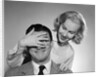 1950s woman standing behind man with hand over his eyes by Anonymous