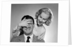 1950s woman standing behind man with hand over his eyes by Anonymous