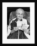 1960s elderly woman in polka-dotted dress & shawl reading letter by Anonymous