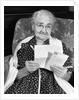 1960s elderly woman in polka-dotted dress & shawl reading letter by Anonymous