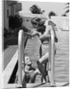 1930s woman wearing one piece bathing suit climbing out of swimming pool looking down at man smiling by Anonymous