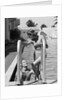 1930s woman wearing one piece bathing suit climbing out of swimming pool looking down at man smiling by Anonymous