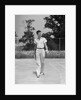 1930s man walking across tennis court holding tennis racket & balls by Anonymous