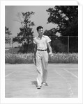 1930s man walking across tennis court holding tennis racket & balls by Anonymous