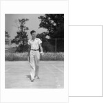 1930s man walking across tennis court holding tennis racket & balls by Anonymous