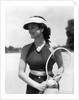 1930s woman in polka dot halter top shorts & sun visor holding a tennis ball & racket by Anonymous