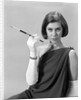1960s formally elegantly dressed young woman looking at camera with a cigarette holder wearing long white gloves by Anonymous