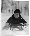 1930s young smiling boy on sled in snow looking at camera by Anonymous