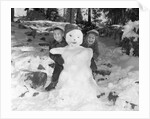 1950s 1960s smiling boy and girl building a snowman together in snowy woods by Anonymous