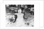 1950s 1960s smiling boy and girl building a snowman together in snowy woods by Anonymous