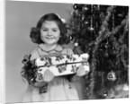 1940s little girl standing near christmas tree holding a wrapped present smiling looking at camera by Anonymous