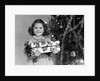 1940s little girl standing near christmas tree holding a wrapped present smiling looking at camera by Anonymous