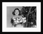 1940s little girl standing near christmas tree holding a wrapped present smiling looking at camera by Anonymous