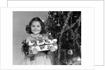 1940s little girl standing near christmas tree holding a wrapped present smiling looking at camera by Anonymous