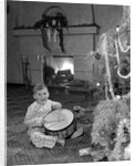 1950s little boy playing toy drum by christmas tree and fireplace looking at camera by Anonymous