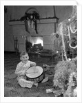 1950s little boy playing toy drum by christmas tree and fireplace looking at camera by Anonymous