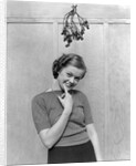 1930s 1940s cute young woman standing under mistletoe smiling hand near mouth looking at camera by Anonymous